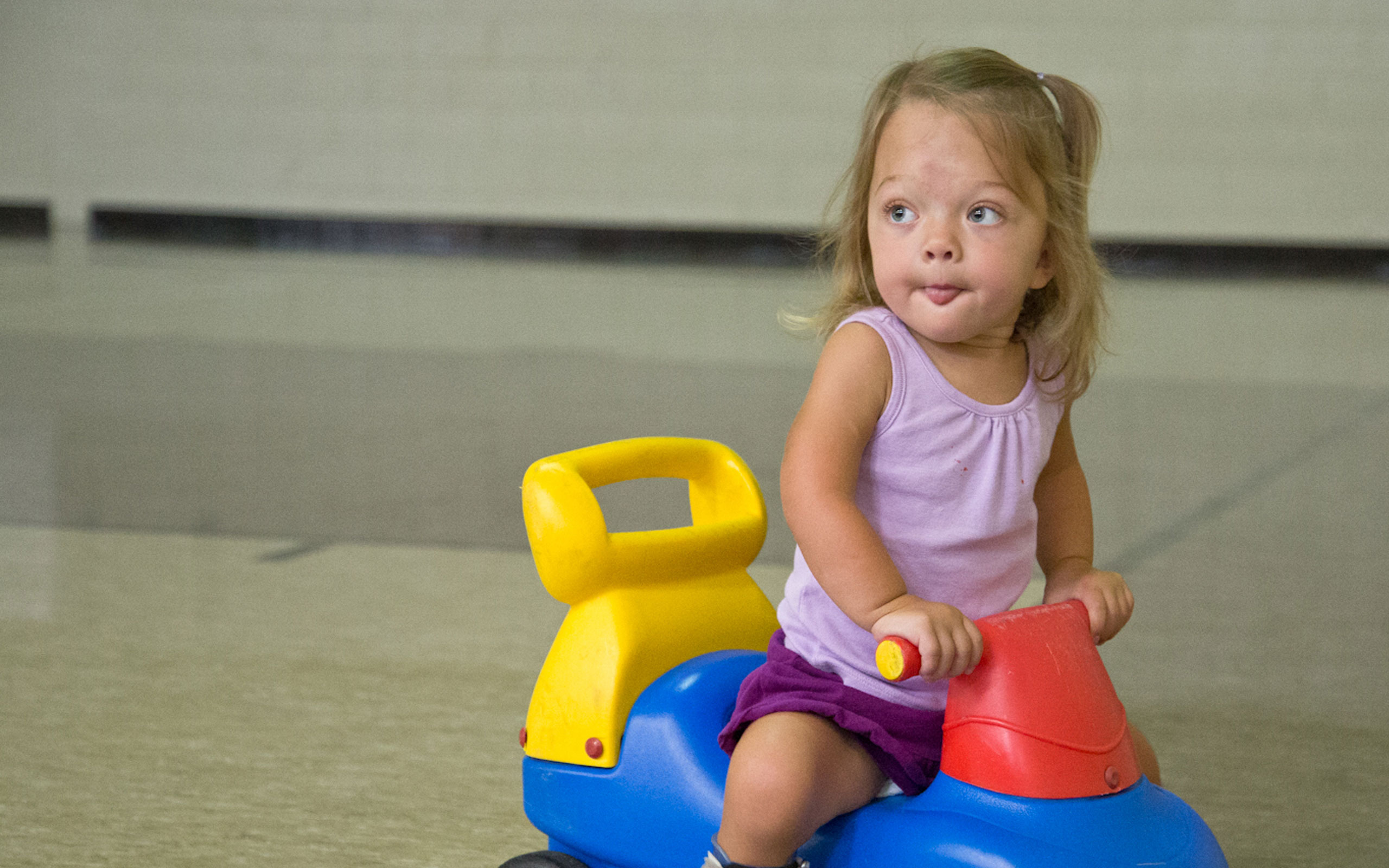 Evie, diagnosed with HPP at 2 weeks old, riding a toy car